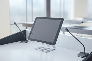 Rostrum with digital tablet and microphone in conference hall.