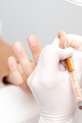 Professional manicure master drawing decorations by pink gel pencil on edge of a nail of young female