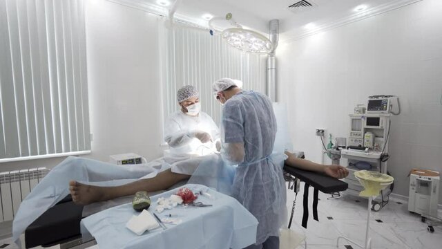 Gallbladder removal operation in the operation theatre. Action. Doctors helping patient during the surgery, bloody bandage is lying on the sterile table.
