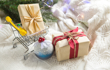 Box with a gift in Christmas packaging in shopping cart on white knitted blanket. Black Friday, buying gifts for new year. Holiday decor, Bank plastic card - cashless payment, online store. Copy space