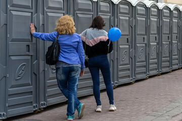 view from the back of two women standing at a row of toilets