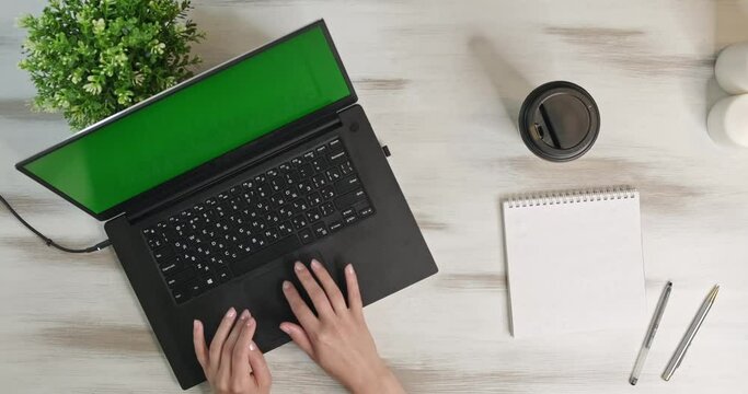Above shot in move woman using laptop computer on office table background. Girl makes notes and typing on laptop keyboard top view. Camera moves slowly over wooden white table laptop with green screen