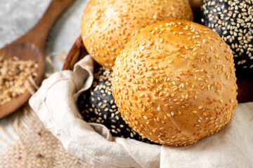 Sesame buns for burgers. Wheat and rye buns in a basket on a light gray background. Homemade buns with sesame seeds. Baking close-up	