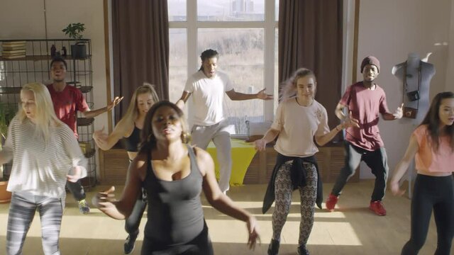 Crane shot of diverse group of people practicing house dance moves in airy studio