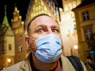Adult man wearing mask walking in a night european city. Mask is a necessary thing in new normal...