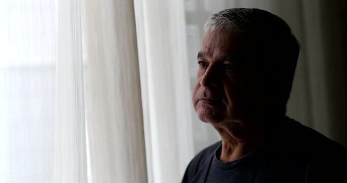 Depressed senior man standing in shadows by window