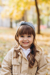 Happy and beautiful little girl in a beige coat walks in the autumn park