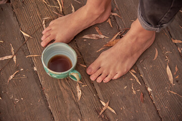 Women's bare feet stand on a wooden floor covered with autumn leaves.