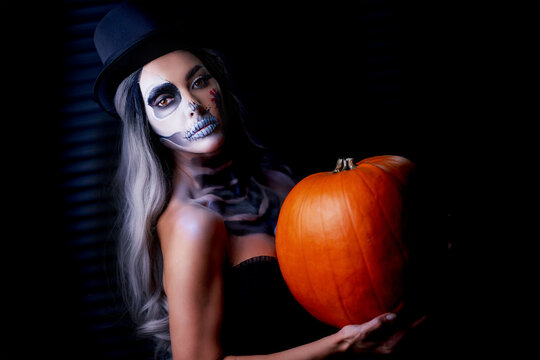 Spooky portrait of woman in halloween gotic makeup holding pumpkin
