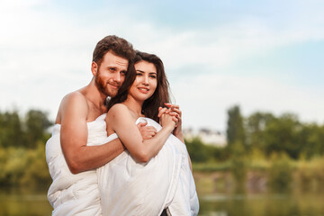 happy couple resting on the lake shore. hug and greet by the dawn wrapped in blankets.