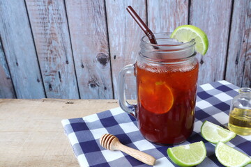a glass of iced lemon tea with honey is put on the wooden table with background of wooden wall of the kitchen during party with happy family