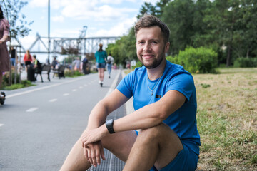 handsome male athlete in blue sportswear looks directly at the camera and smiles after an outdoor workout.