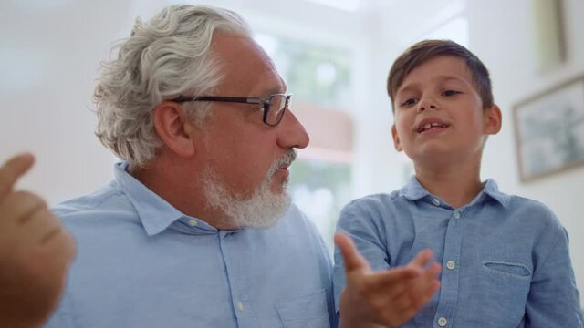 Grandfather talking grandson in room. Cheerful boy sitting on grandparent laps