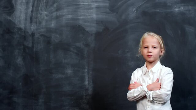 Portrait shot of confident little girl with blond hair standing with her arms crossed and looking at camera