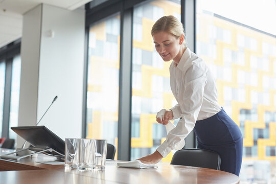 Portrait Of Elegant Young Woman Cleaning Table In Conference Room With Sanitizing Spray While Preparing For Business Event In Office, Copy Space