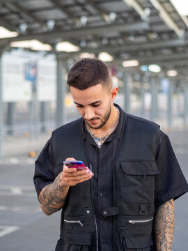 Hombre joven con tatuajes hablando por tel&eacute;fono por la calle durante la puesta de sol