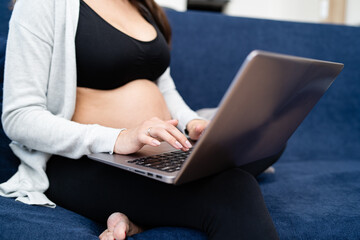 Pregnant woman wearing sports clothes sits on the couch in the living room and checks her email while waiting for the lab test results.