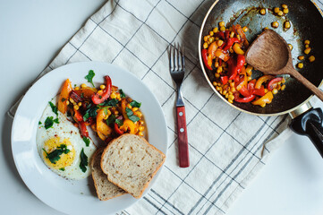 tasty vegetarian farm style breakfast - fried egg with baked sweet peppers and corn with parsley and whole grain bread served on white plate