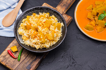 Curry or pumpkin soup with rice served in a ceramic platter on a black background - top view with writing space.