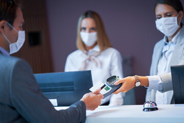 Businessman in mask at the reception desk of a hotel checking in