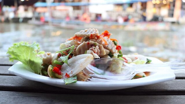 The spicy vietnamese sausage salad on dish with blurred of motion boat at background, Khlong Lat Mayom Floating Market, Thailand.