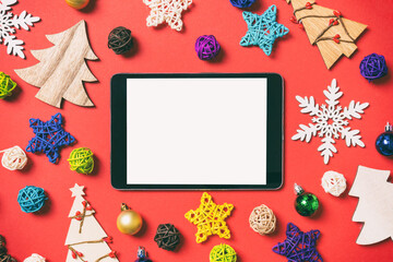 Top view of digital tablet on red background made of holiday decorations and toys. Christmas ornament concept