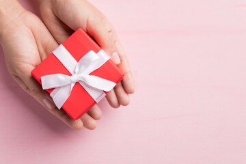 Red gift box with white ribbon holding by hand on pink background, Present for giving in special day, Top view