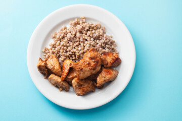 boiled buchwheat with chicken in sauce on white plate on blue background