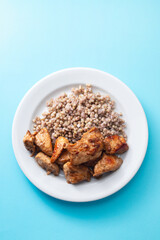 boiled buchwheat with chicken in sauce on white plate on blue background