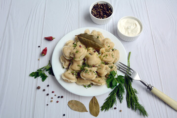Dumplings in the form of hippos on a white dish with greens, pepper and bay leaf on a light wooden background