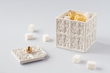 White sugar bowl with sugar cubes inside and golden candies. Dessert, sweets, candies conceptual image. Luxury, tea party, sweets