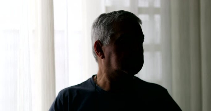 Depressed senior person in shadows at home. Older retired man standing at home