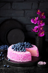 Obraz na płótnie Canvas Homemade crepe cake with pink coconut pitahaya cream and fresh blueberries on a black background, selective focus
