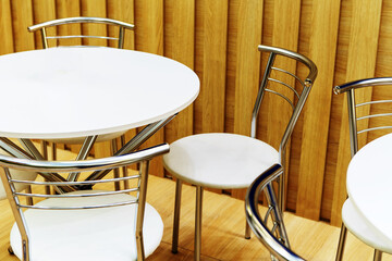 Tables and chairs white on the background of a wooden wall. Interior of a fast food cafe. Close-up.