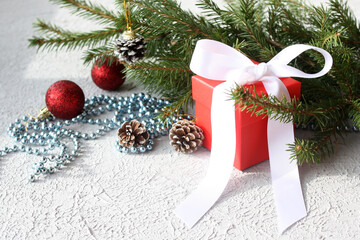 There is a Christmas present in a red box under the tree. Christmas balls, fir cones and shiny beads and a gift on the background of the Christmas tree. Selective focus,