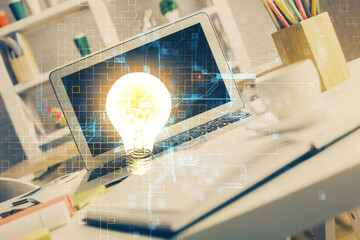 Computer on desktop in office with bulb icon hologram. Double exposure. Concept of idea.
