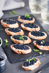 Toasts with black caviar and two glasses of white wine on grey stone background