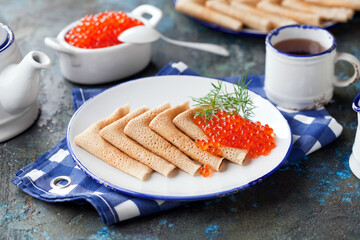 Traditional Russian pancakes with red caviar on a plate, selective focus