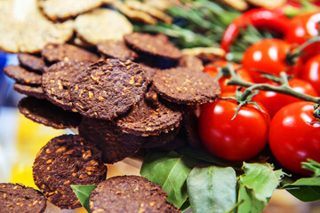 Rye cookies with nuts and sesame seeds decorated with red tomatoes. Healthy food made from flour and vegetables. Close-up