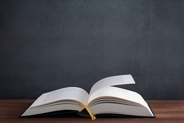 Open book on dark wooden table against grey stone background, copy space
