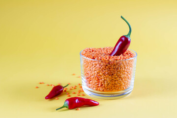 Red lentils in a glass jar with red chili peppers on a yellow background. Healthy food concept,...