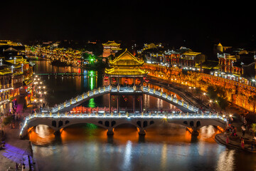 Beautiful night scenery and Fenghuang Bridge of Fenghuang (Phoenix) ancient town, Hunan province, China. Cityscape at night with reflection light in the river.