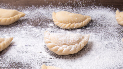 Homemade dumplings, vareniki on an old wooden table, sprinkled with flour, space for text