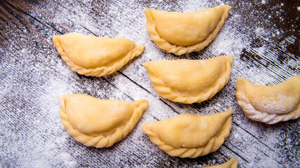 Homemade dumplings, vareniki on an old wooden table, sprinkled with flour, space for text