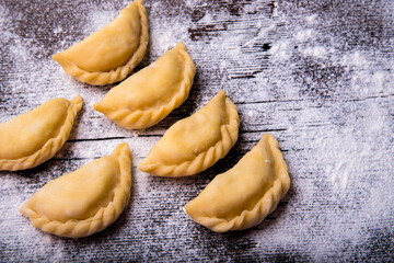 Homemade dumplings, vareniki on an old wooden table, sprinkled with flour, space for text