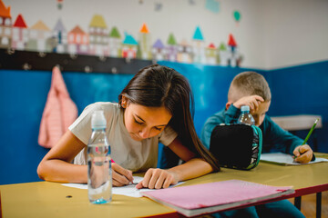 Elementary schoolchildren writing at the desk in the classroom.