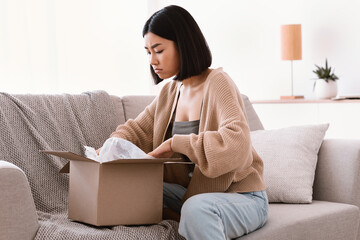 Confused young woman unpacking wrong parcel, delivery mistake