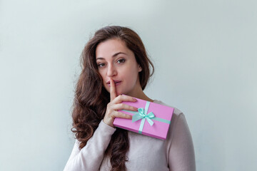 Young positive woman holding small pink gift box isolated on white background. Preparation for holiday. Girl looking happy and excited. Christmas birthday valentine celebration present concept.