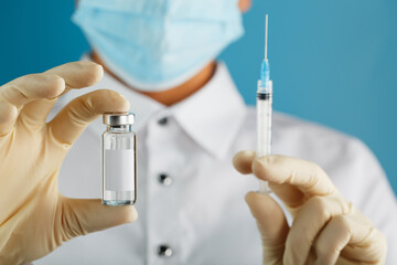 A doctor in rubber gloves holds an ampoule with a vaccine and a syringe, close-up.