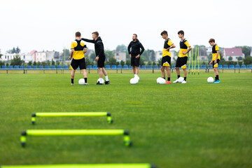 Obraz na płótnie Canvas Soccer Team on Training. Group of Young Football Players With Coaches on Grass Practice Field. Young Coach Explaining Training Game Plan to Team